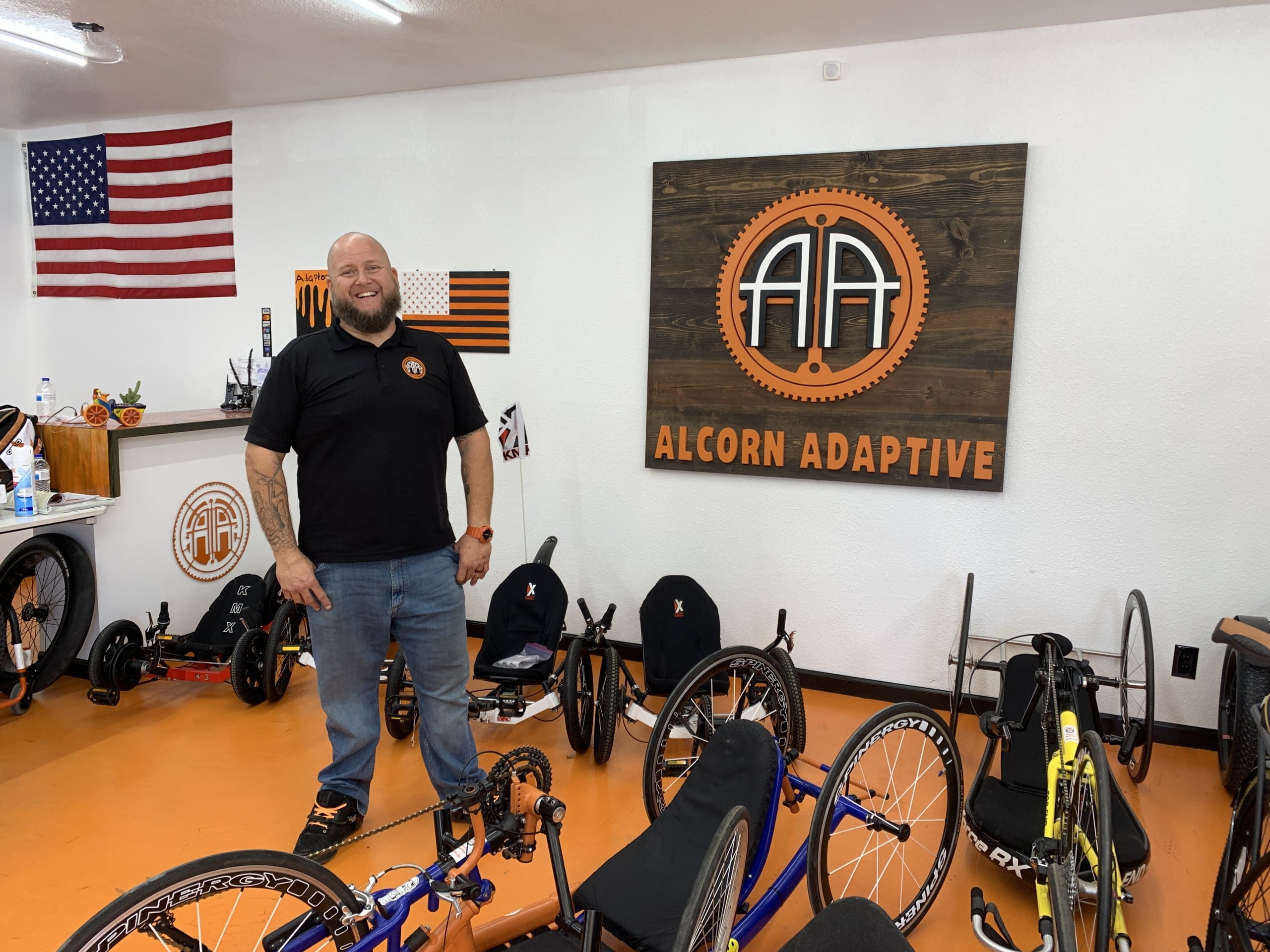 Jerry Alcorn stands smiling inside his shop. There are several different kinds of bikes in front of him